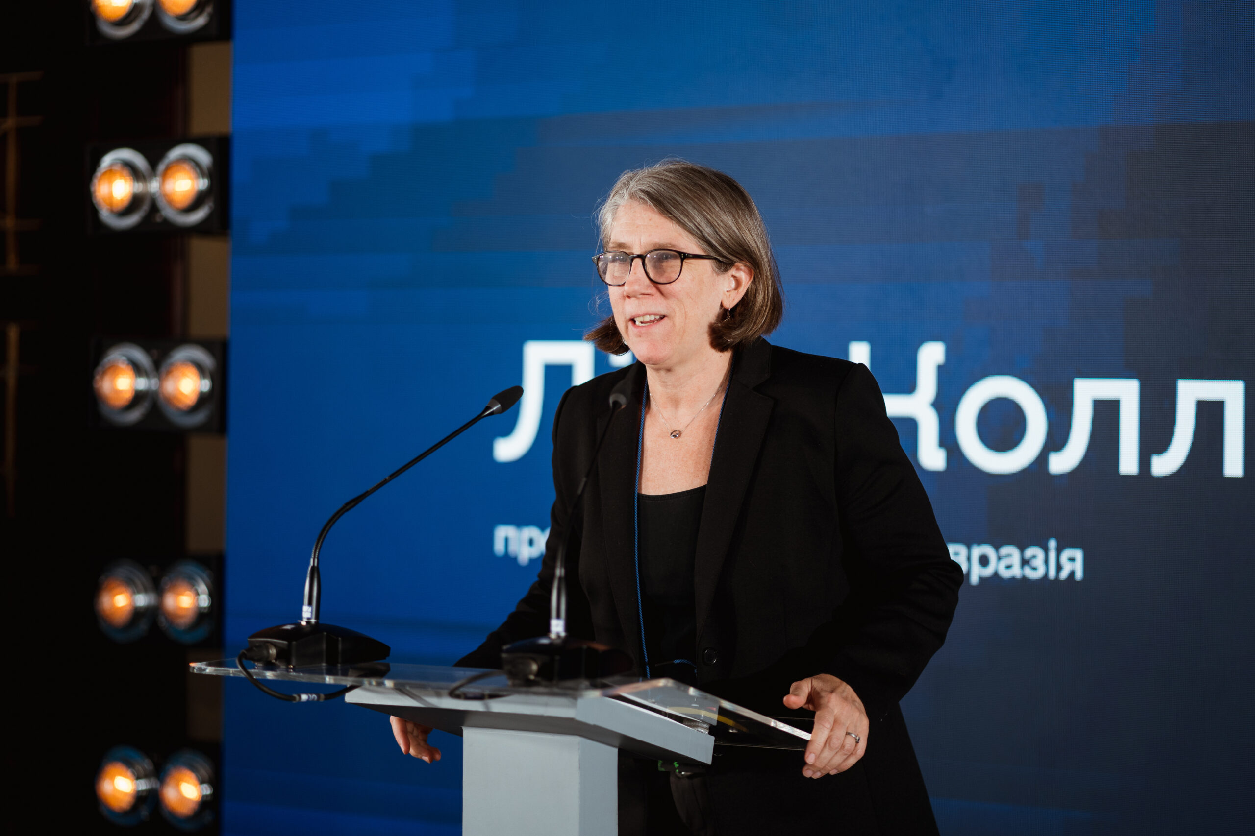 Lisa Coll, EF president, addresses the crowd at the Ukraine Digital Transformation Activity launch event. A screen spanning the stage behind her shows her name in Ukrainian with the USAID and UK Dev logos.