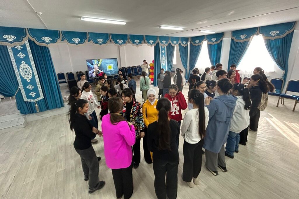 A group of approximately twenty high school age students stand in pairs. The pairs spread out to form two concentric circles.